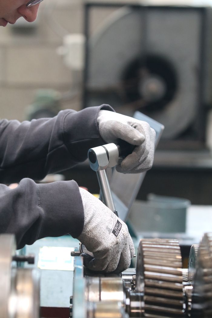 why-choose-us Male worker using tools on machinery in an industrial workshop setting.