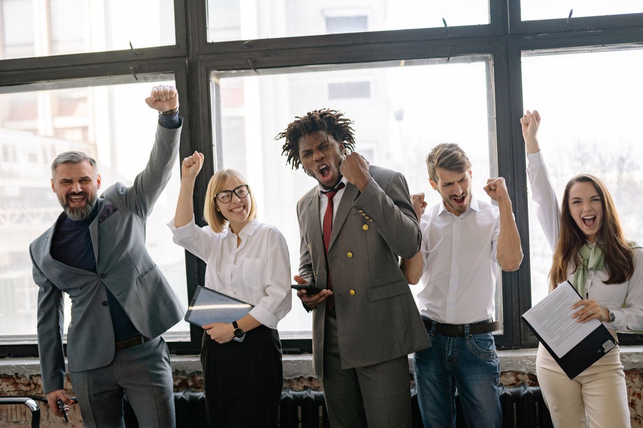 about-01 Group of diverse professionals celebrating achievement in office setting with enthusiasm.