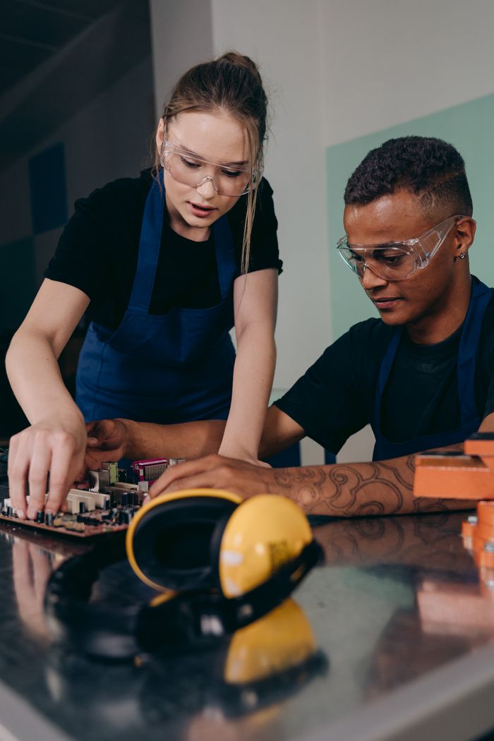 hero-img-02 Two engineers collaborating in a lab, focusing on electronic components wearing safety eyeglasses.